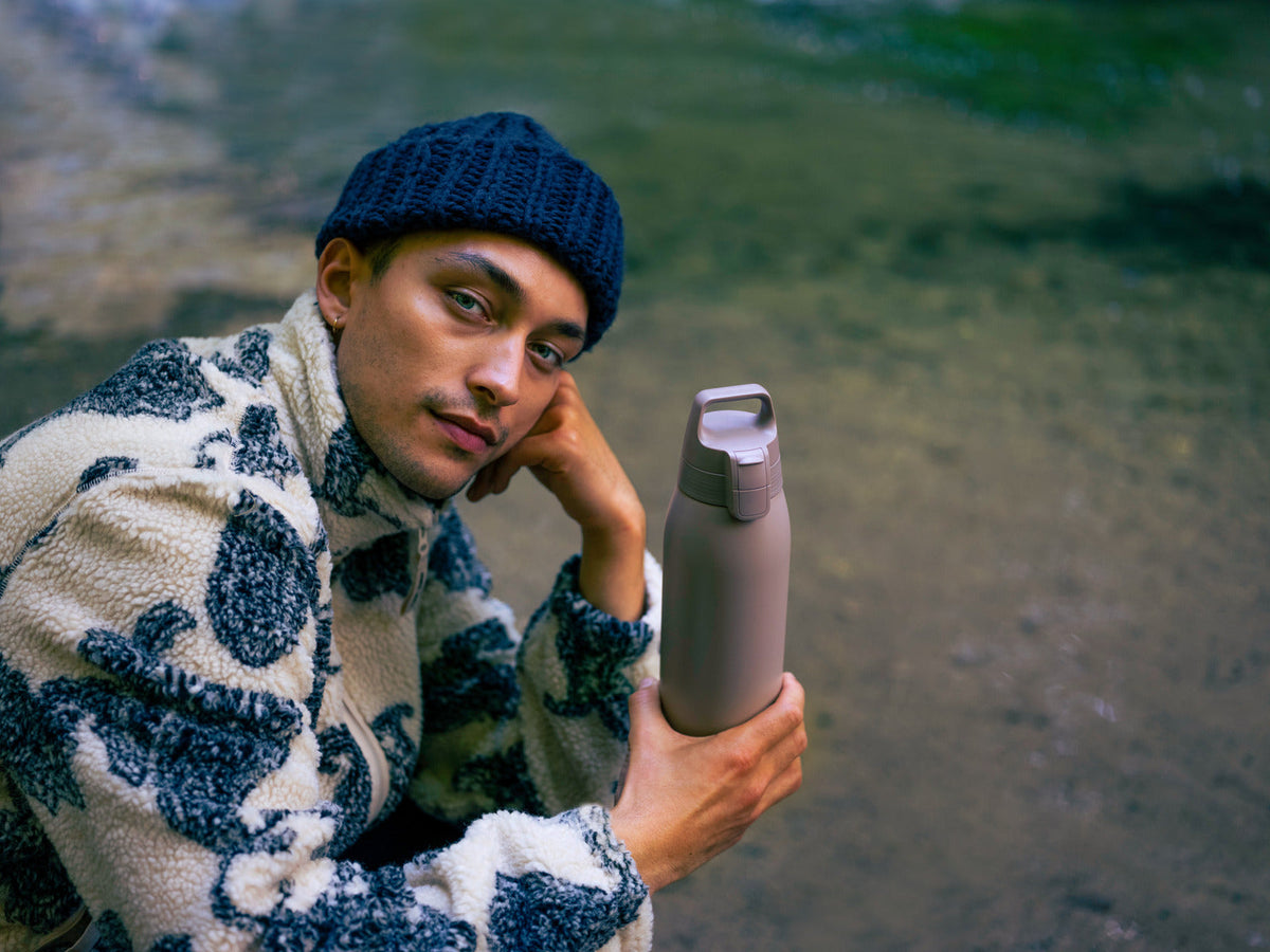 En man i blå mössa och mönstrad fleece håller en SIGG-flaska utomhus